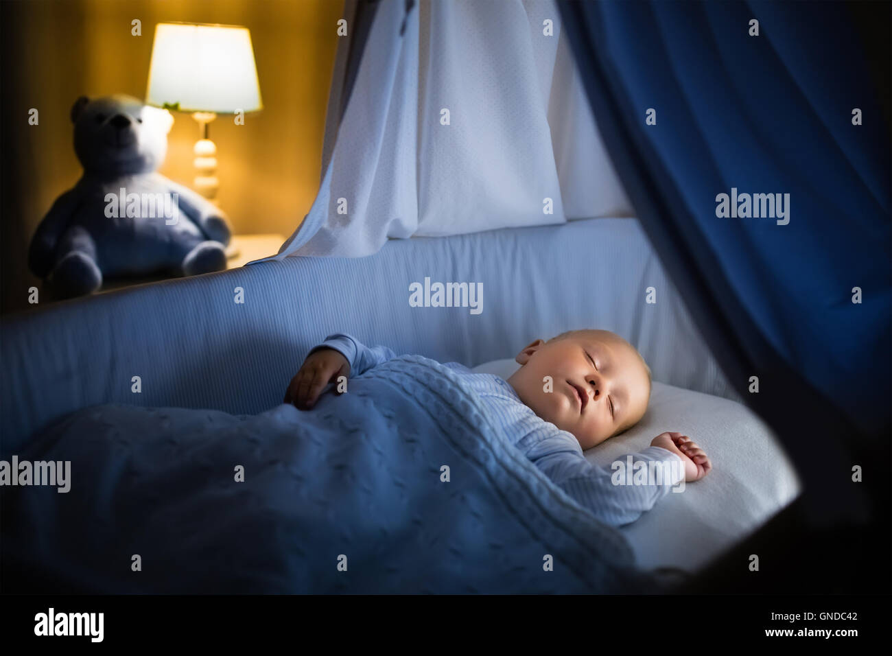Adorable baby sleeping in blue bassinet with canopy at night. Little boy in pajamas taking a nap in dark room with crib Stock Photo Alamy