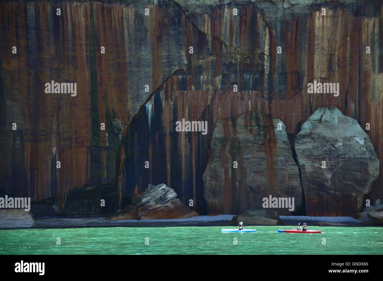 Two kayakers before cliff at Pictured Rocks National Park, MI, USA in front of colored cliff on coast of Lake Superio Stock Photo