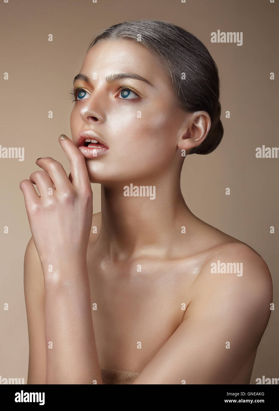Portrait of a woman with golden skin. She looks up, a finger touches the lips. Stock Photo