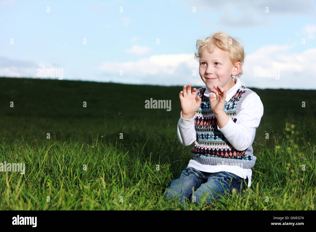 Impish little boy kneeling in green field Stock Photo