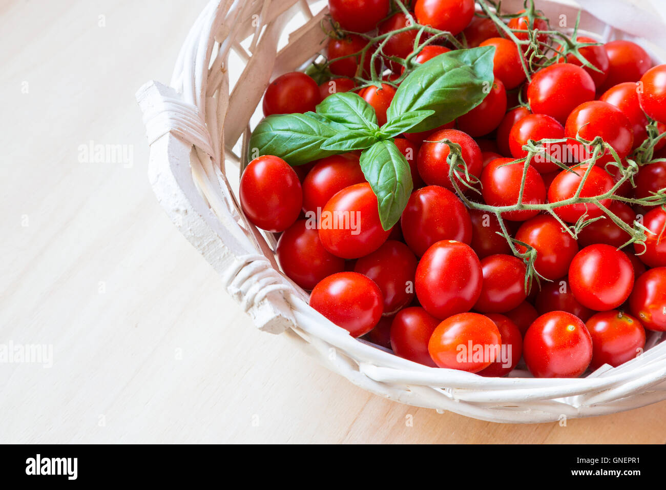 Small red cherry tomatoes in a wicker basket on an old wooden table ...