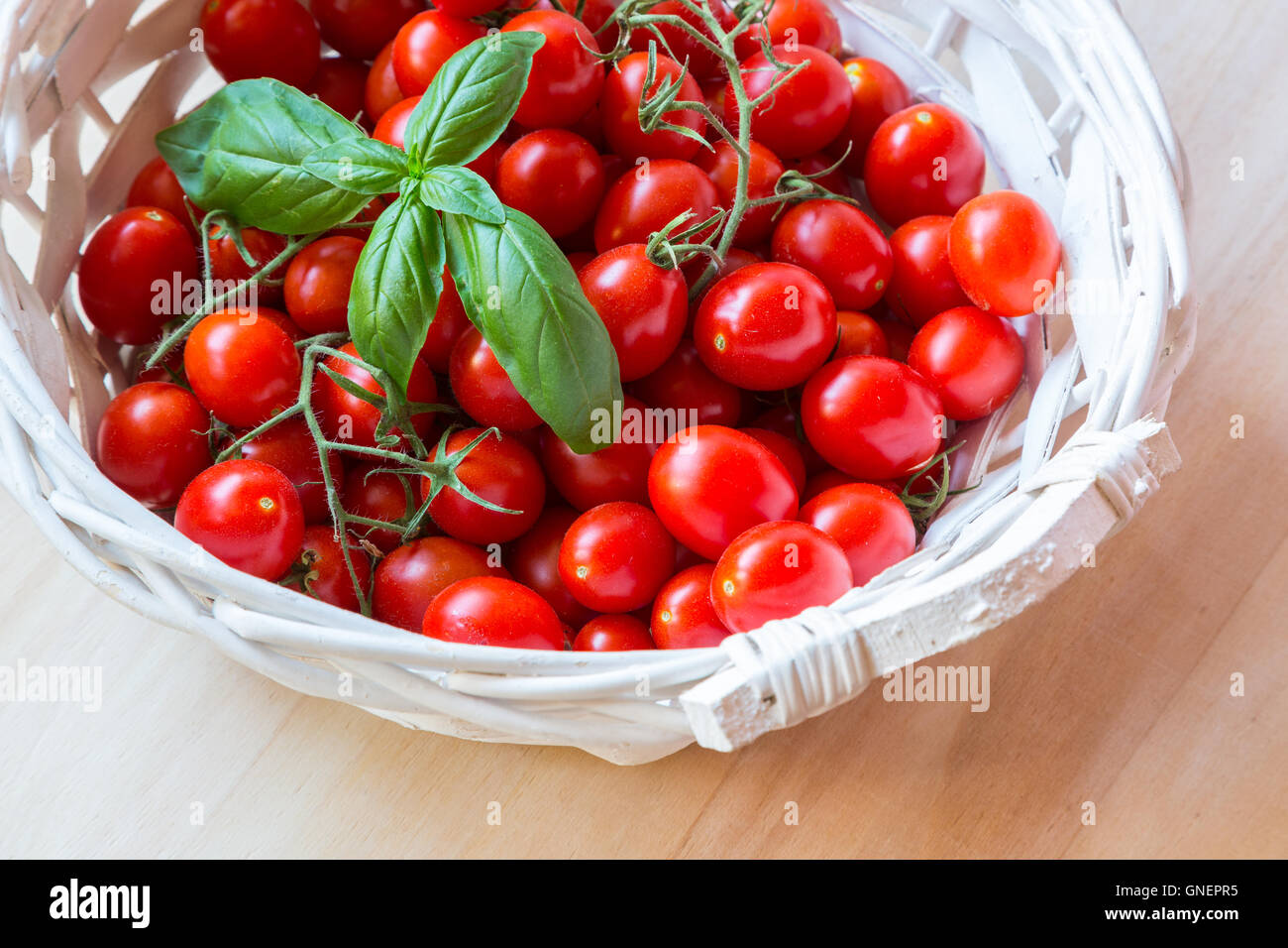 Small red cherry tomatoes in a wicker basket on an old wooden table ...
