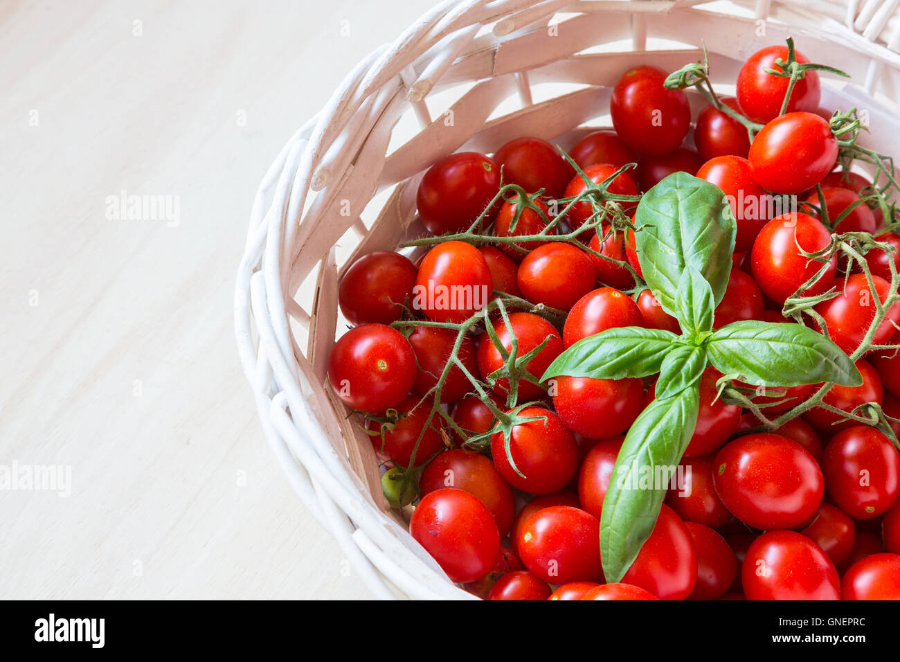 Small red cherry tomatoes in a wicker basket on an old wooden table ...