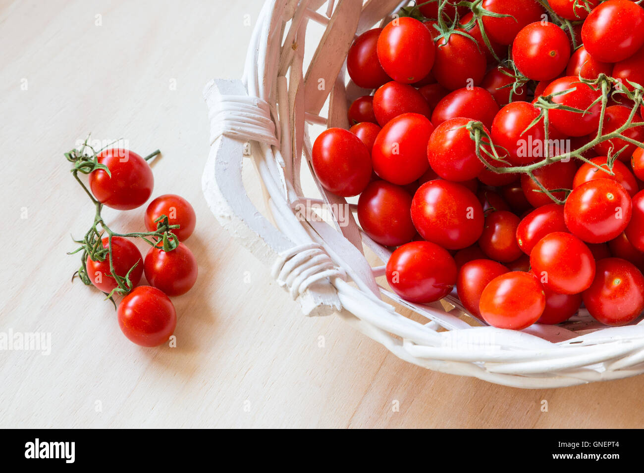 Small red cherry tomatoes in a wicker basket on an old wooden table ...