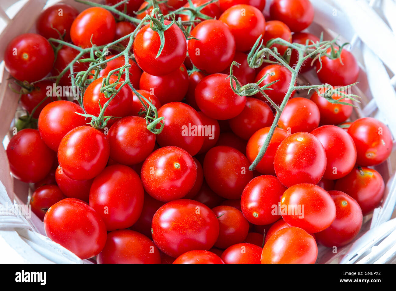 Small red cherry tomatoes in a wicker basket on an old wooden table ...
