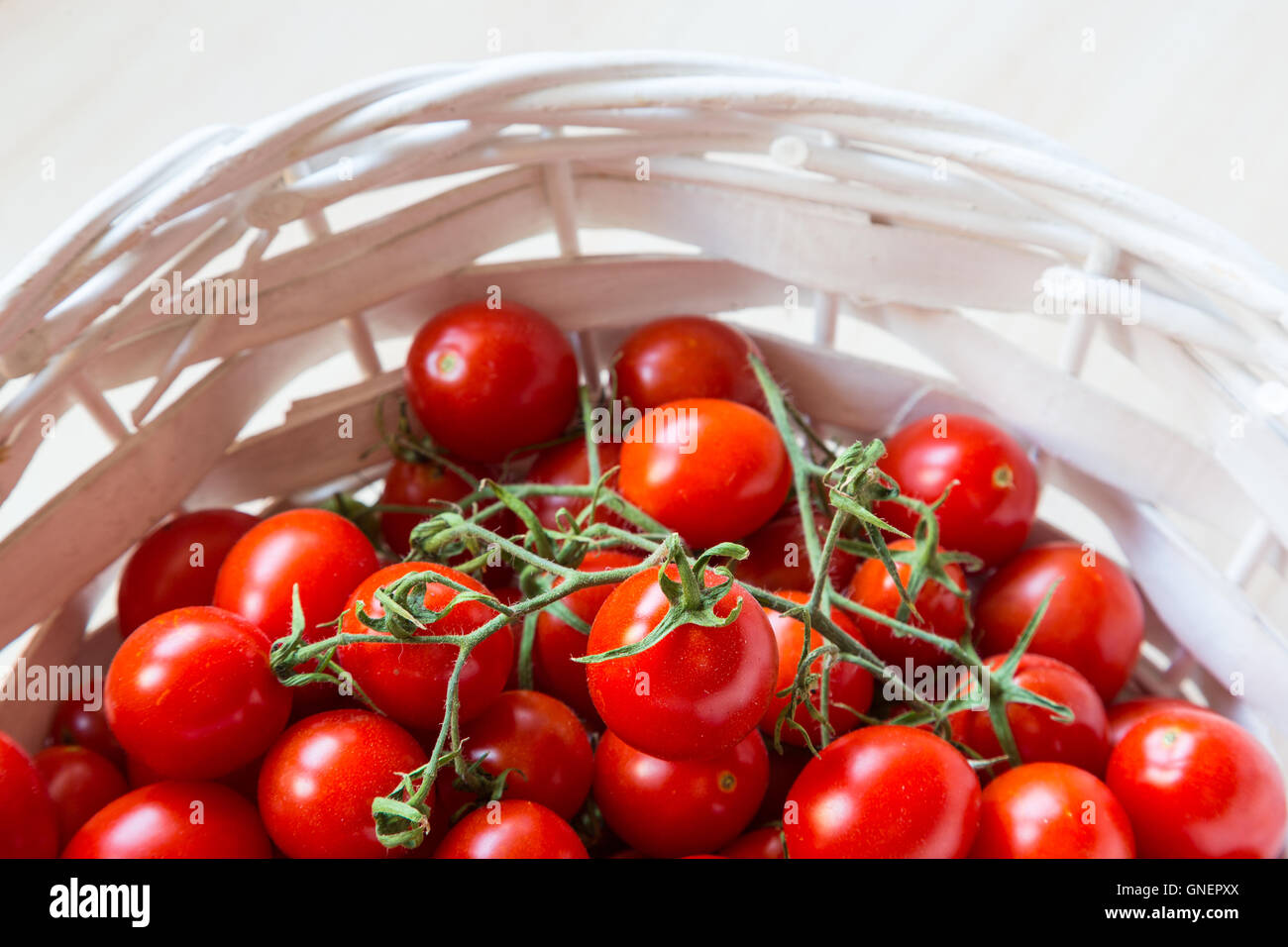 Small red cherry tomatoes in a wicker basket on an old wooden table ...