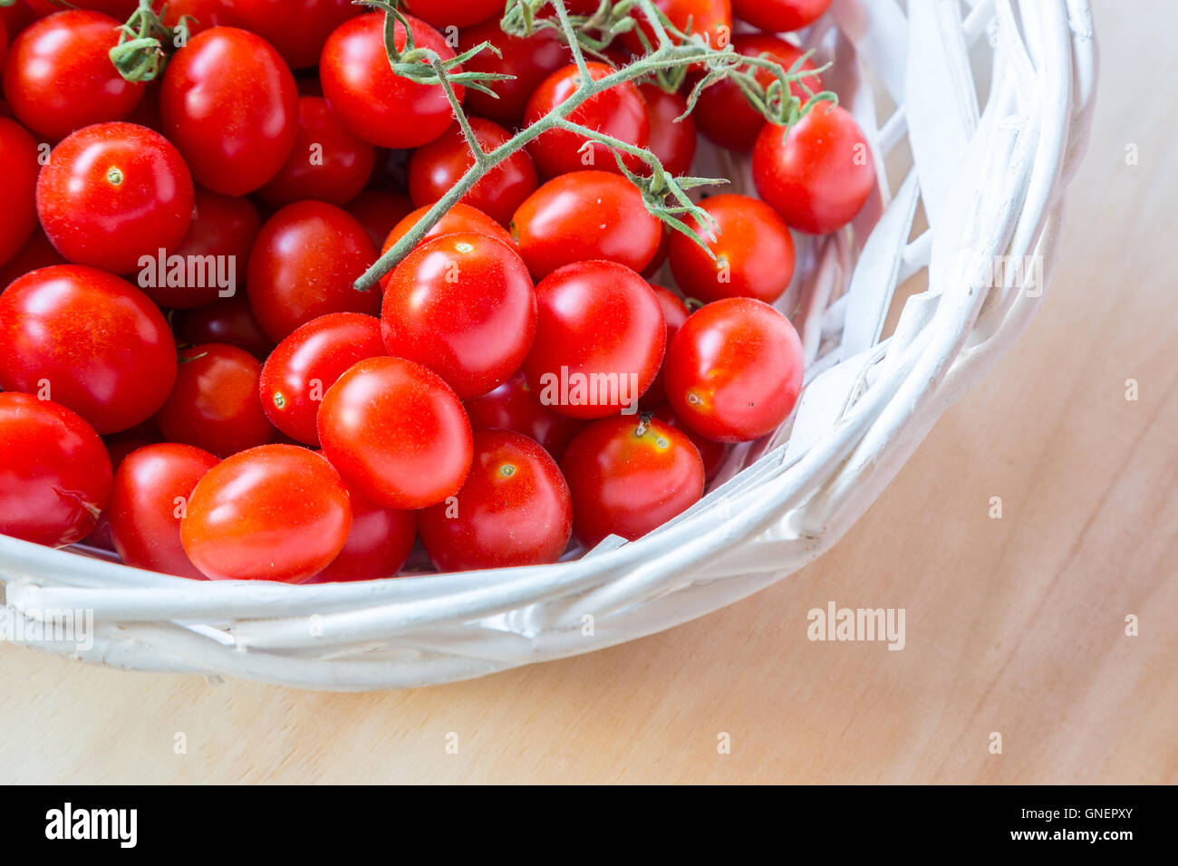 Small red cherry tomatoes in a wicker basket on an old wooden table ...