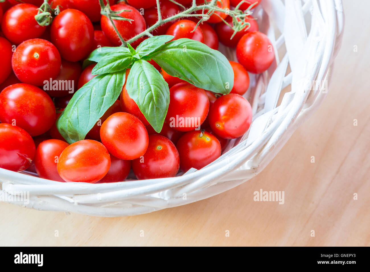 Small red cherry tomatoes in a wicker basket on an old wooden table ...
