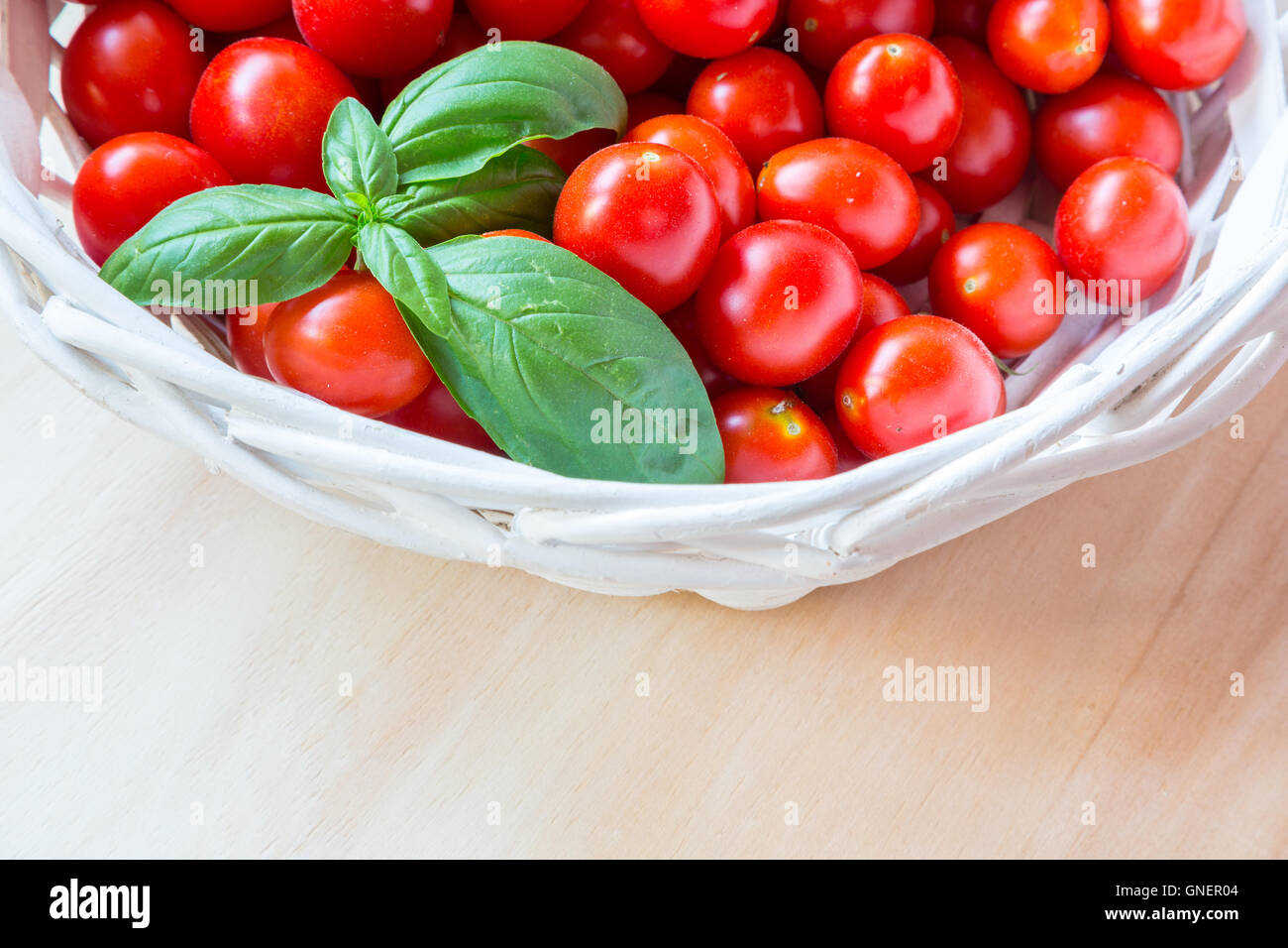 Small red cherry tomatoes in a wicker basket on an old wooden table ...