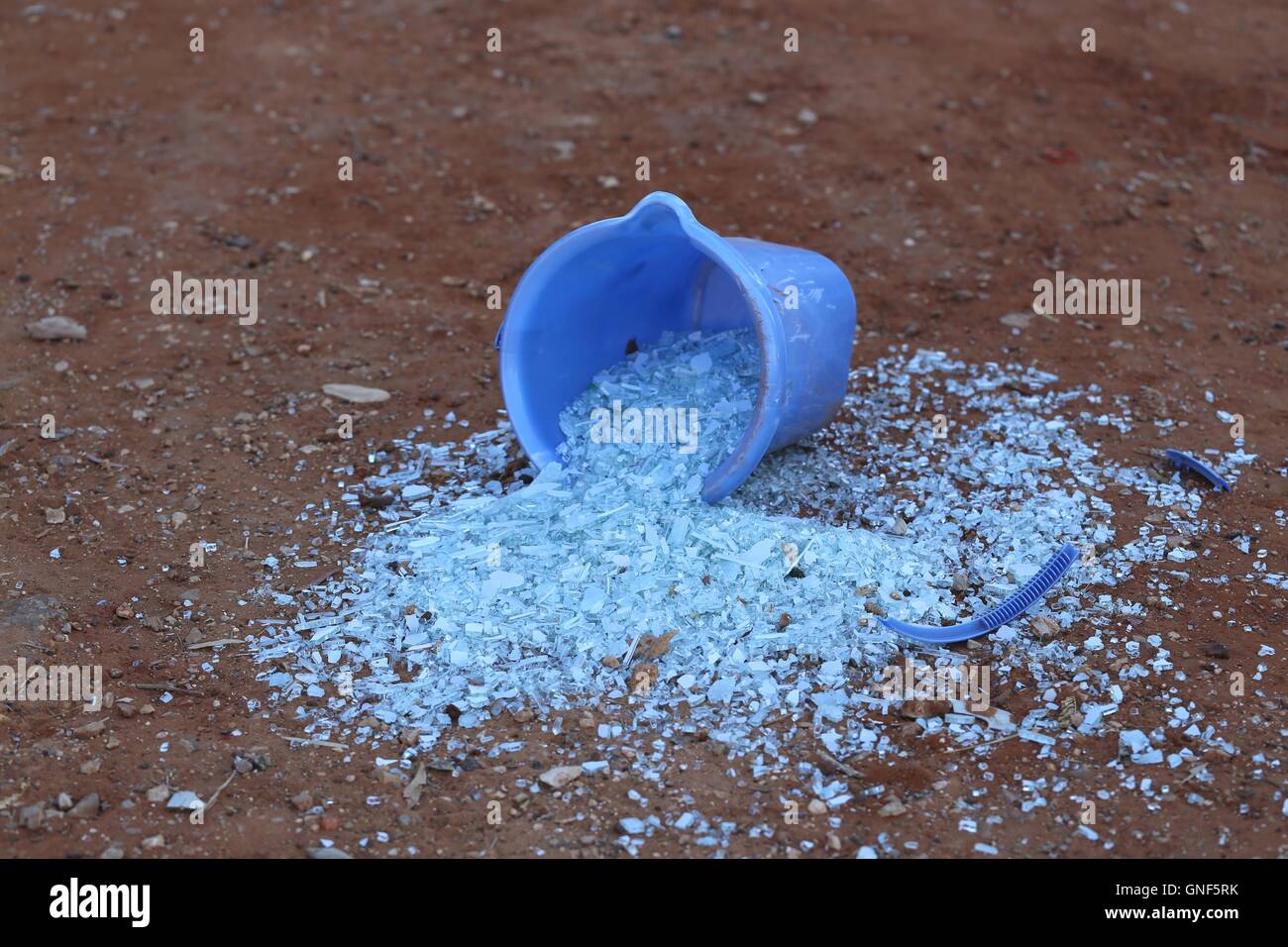 Glass fragments spread from a Bucket. Broken glass pieces spread on the ground out of bucket with broken handle. Stock Photo