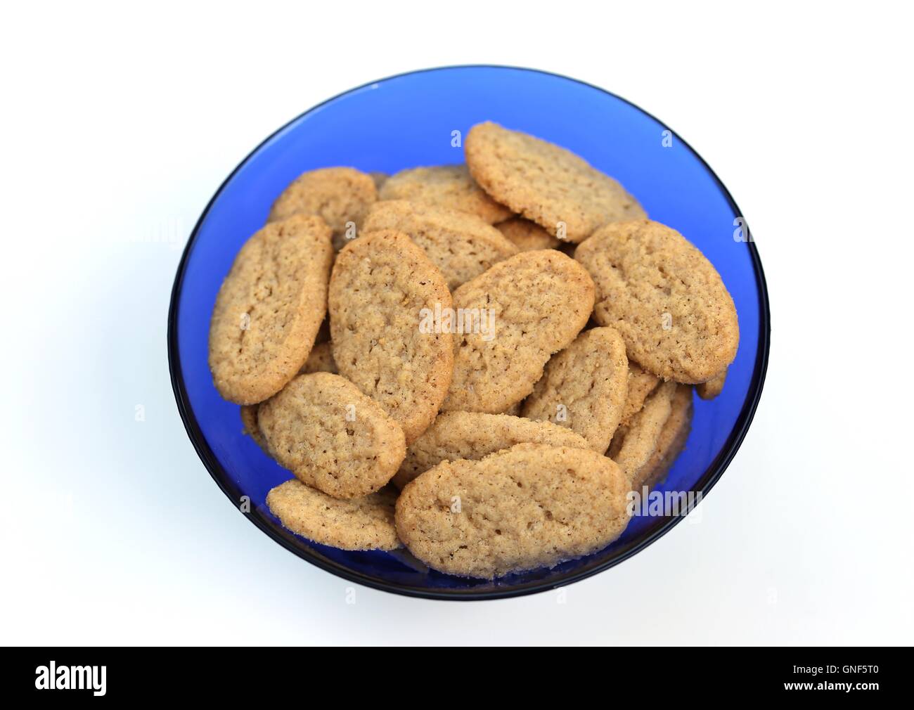 Cookies in a Blue Glass Bowl. Pile of oval homemade butter cookies in a round blue transparent glass dish, isolated on white background, top view. Stock Photo