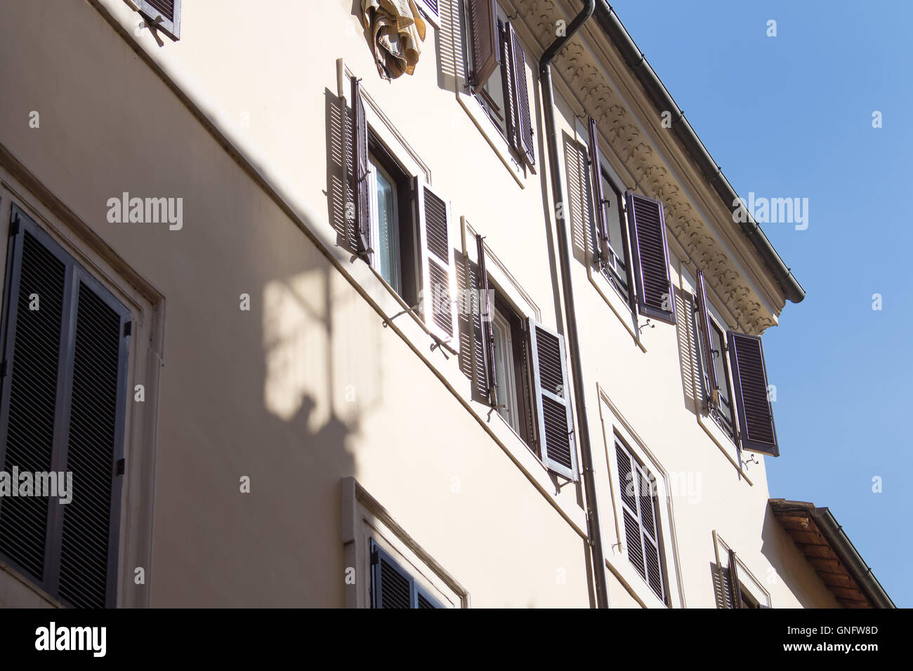 Detail of the roman residential house with enlightened shutters of the windows. Bright blue sky in the background. Stock Photo