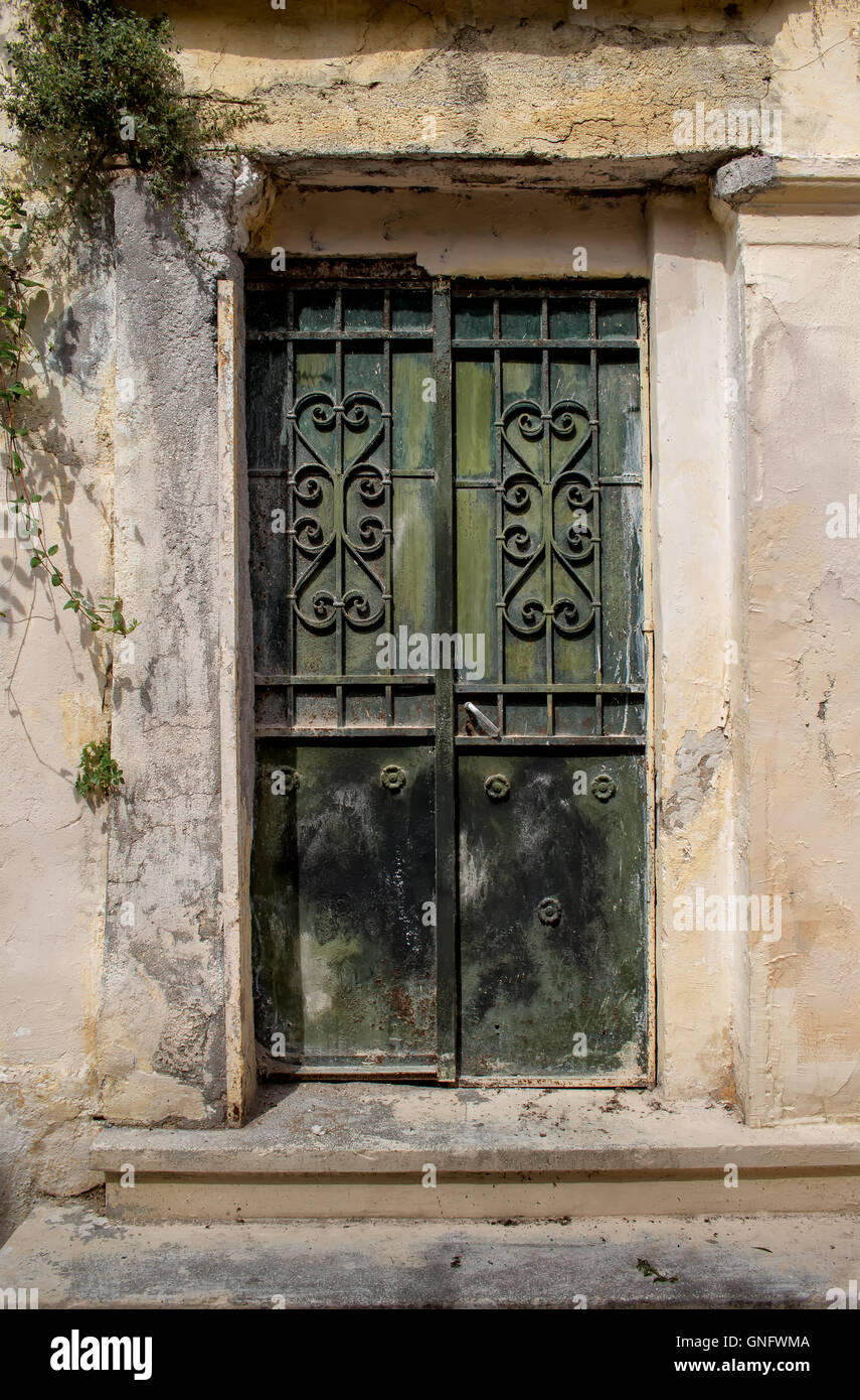 Facade of an old house. Entrance green iron door with a heart design grid. Plant in the corner on the wall. Athens in Greece. Stock Photo