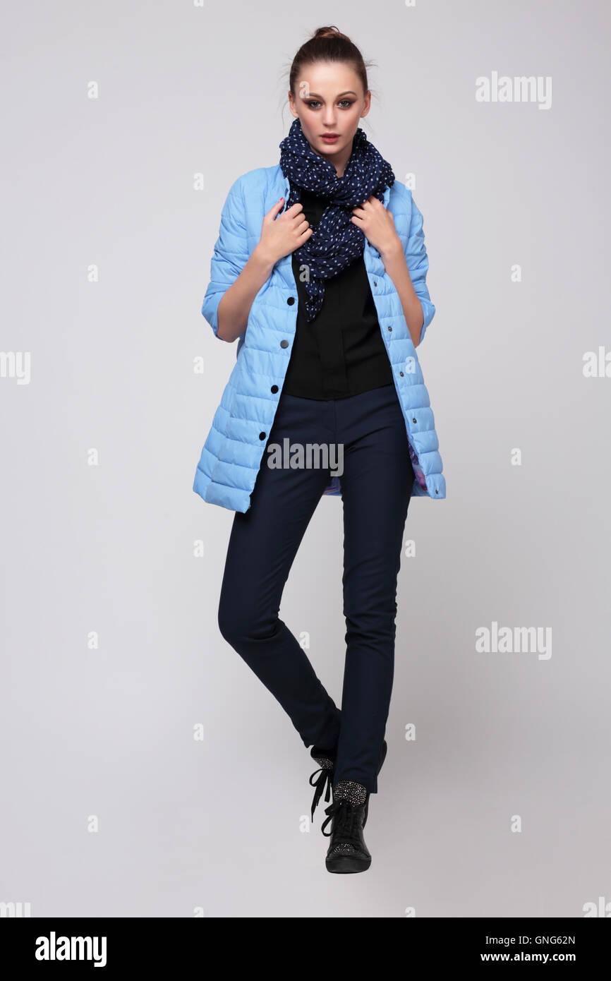 Young woman in a blue jacket with a scarf around his neck and pants, posing in studio full-length. Fashion. Stock Photo