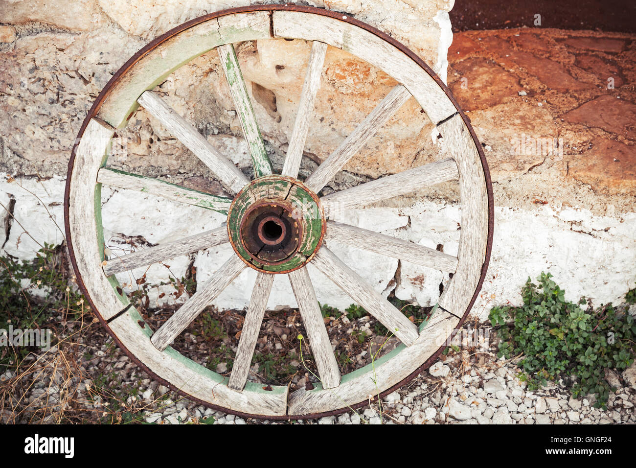 Old wooden wheel stands near stone rural wall Stock Photo