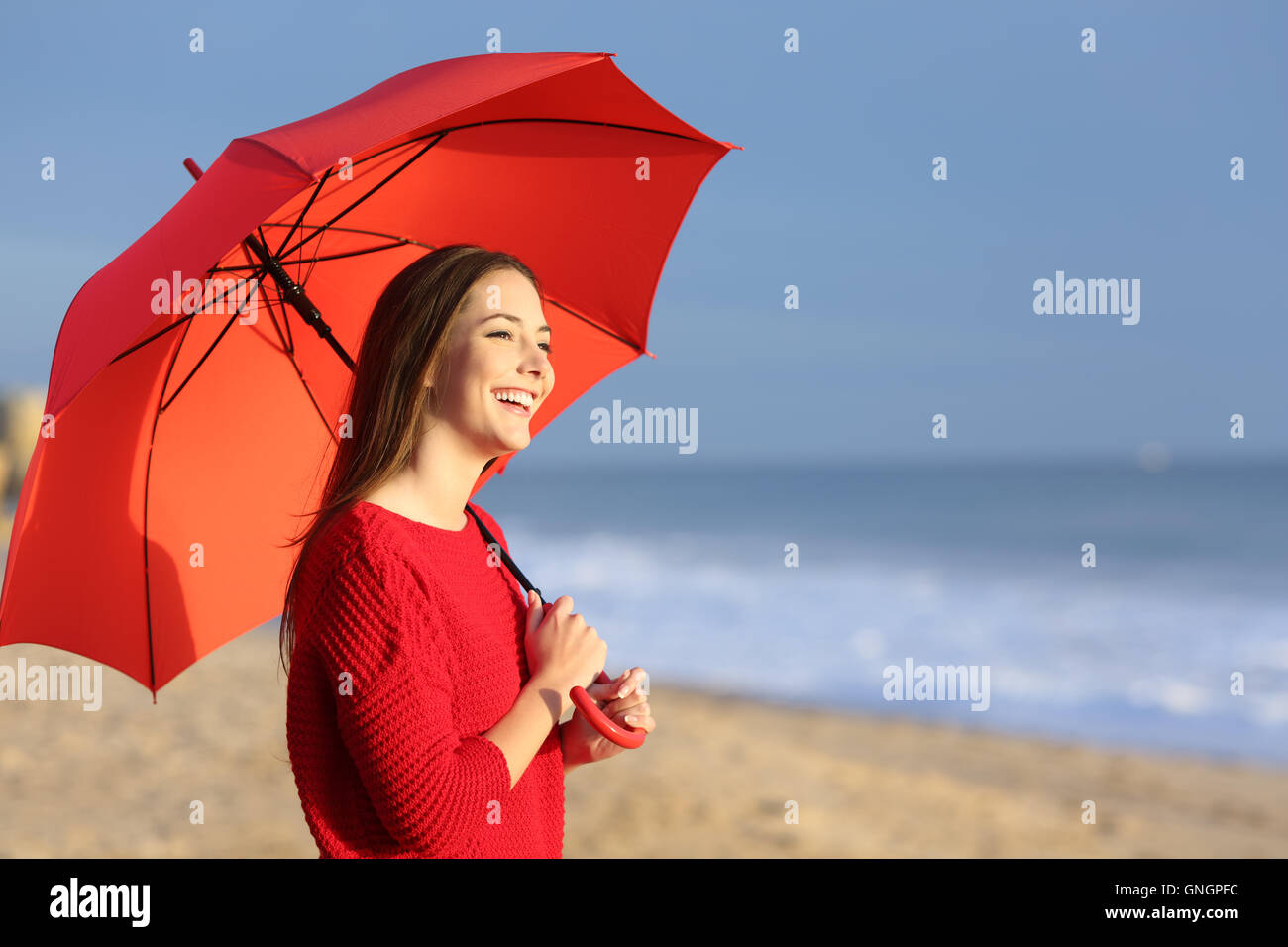 Portrait of a happy girl with red umbrella on the beach at sunset with the horizon and sea in the background Stock Photo
