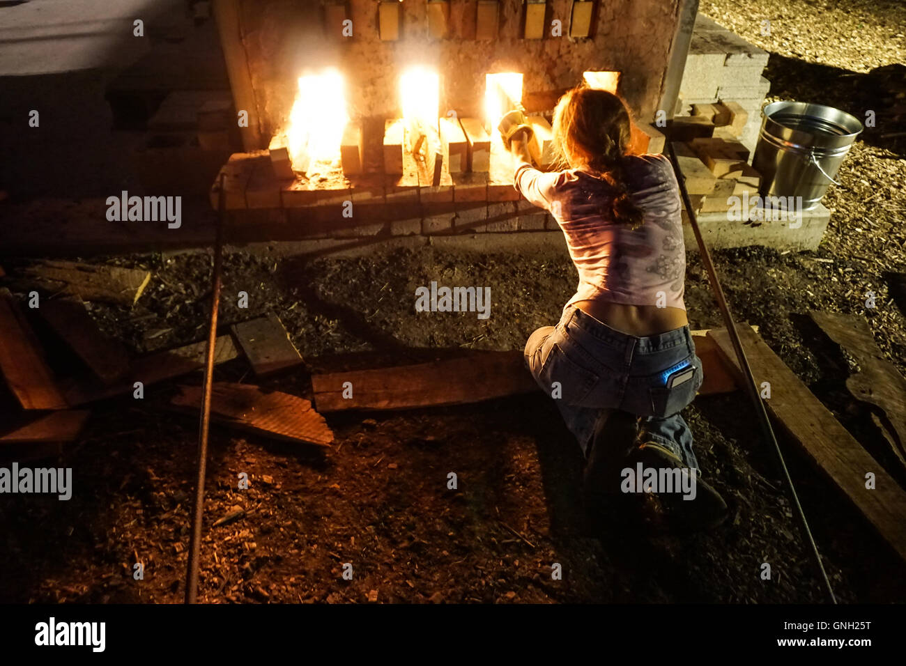 Woman tending to fire of wood kiln at night Stock Photo