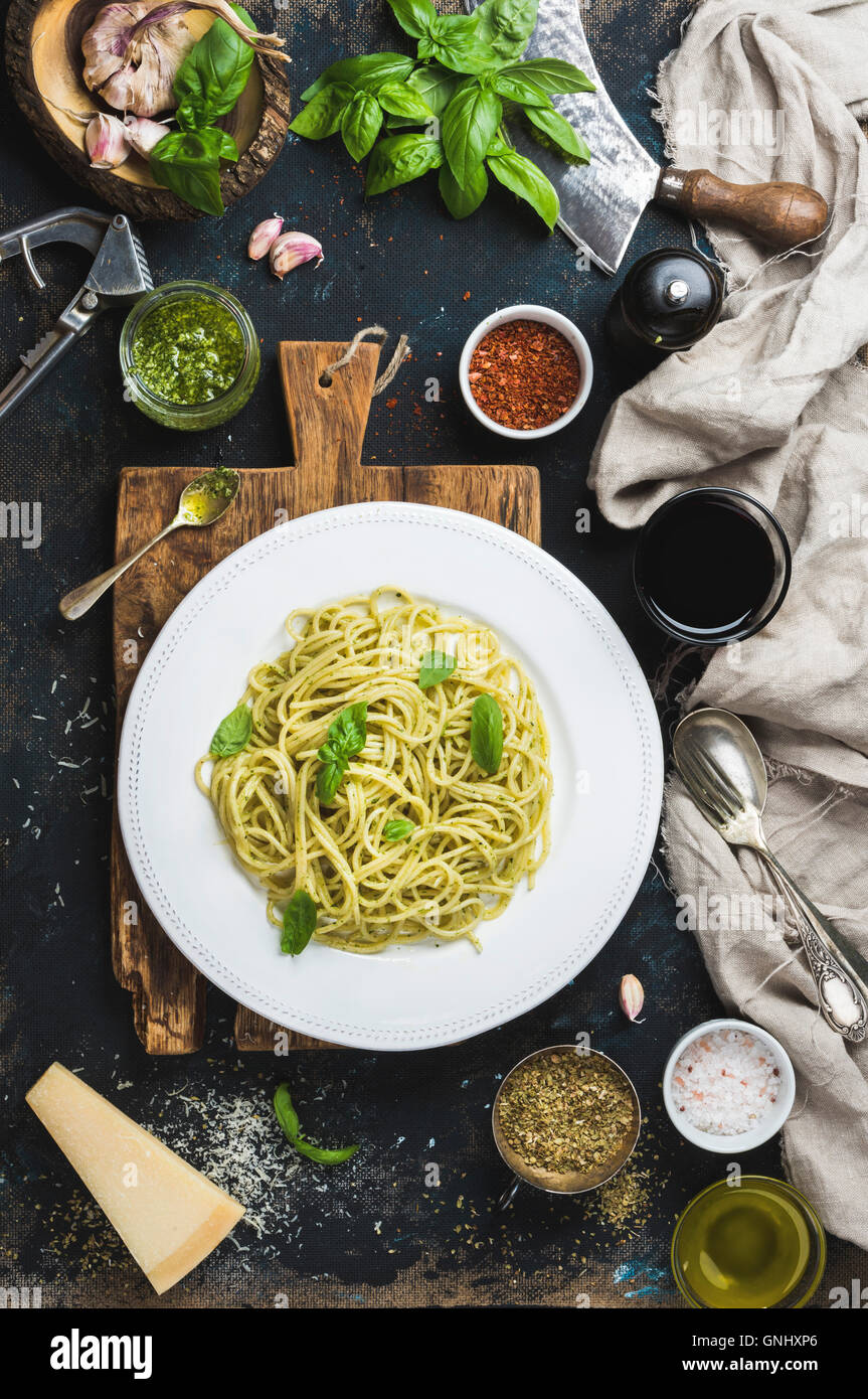 Italian pasta dinner. Spaghetti with pesto sauce and fresh basil, Parmesan cheese and spices served with glass of wine on rustic Stock Photo
