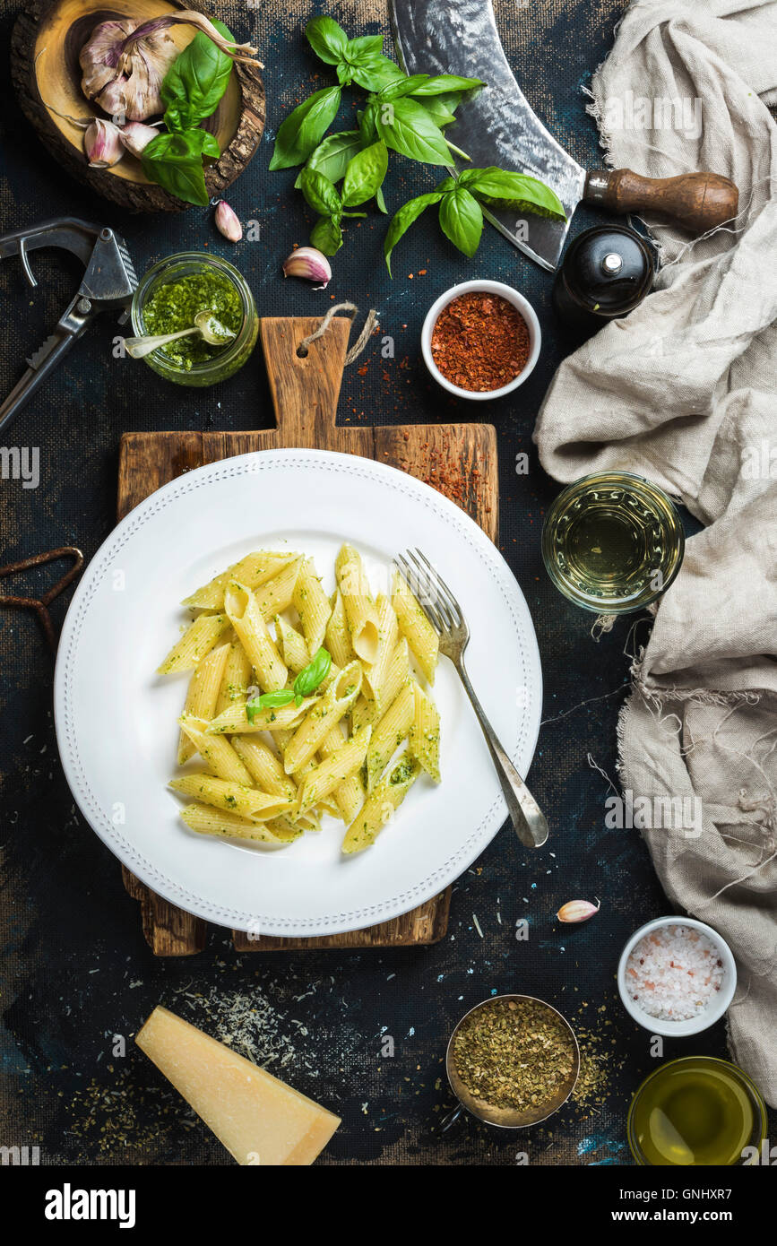 Italian pasta dinner. Penne with pesto sauce and fresh basil, Parmesan cheese and spices on rustic wooden board over dark grunge Stock Photo
