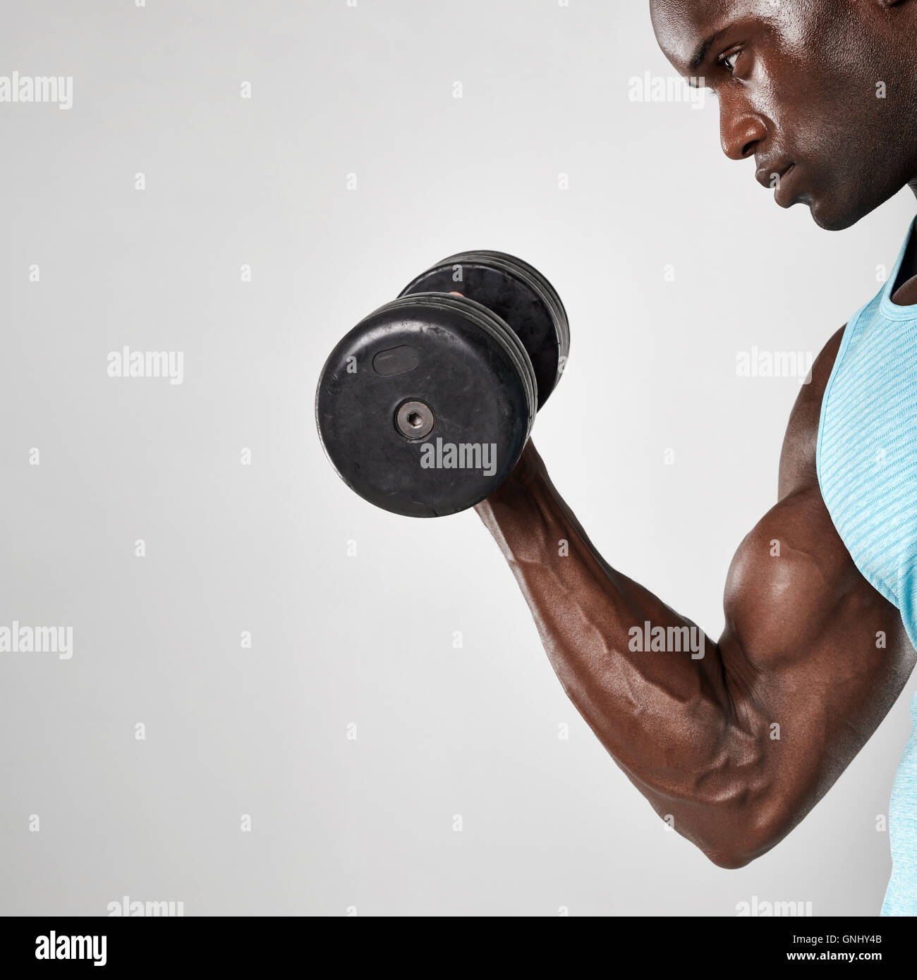 Side view shot of young and muscular african man doing biceps curl with dumbbell against grey background Stock Photo