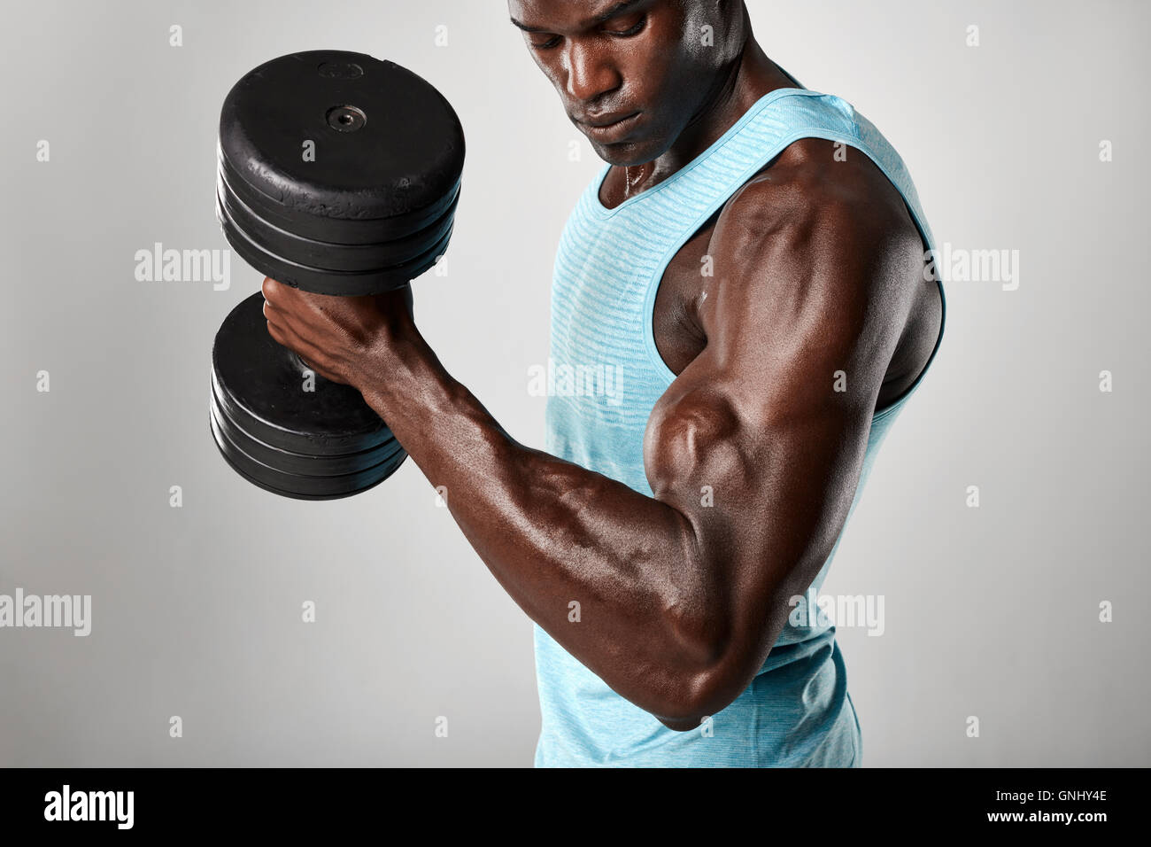 Shot of fit young man doing biceps curl with dumbbell against grey background. African fitness model exercising with heavy dumbb Stock Photo