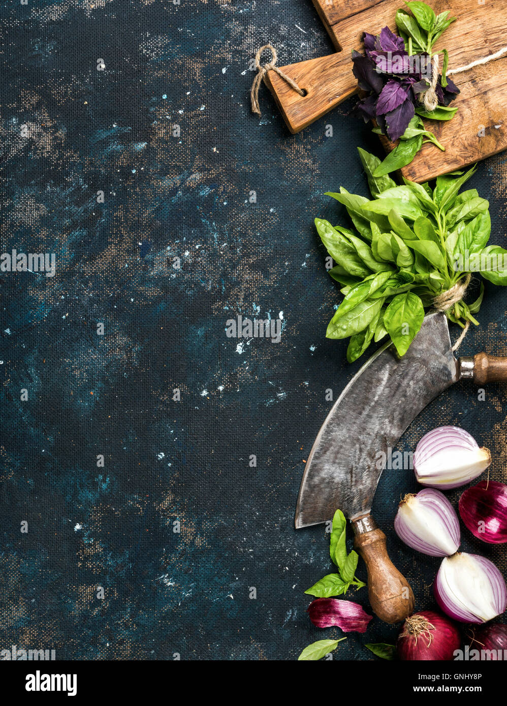 Healthy food cooking background. Fresh green and purple basil leaves, red onions and garlic, herb chopper knife and rustic cutti Stock Photo