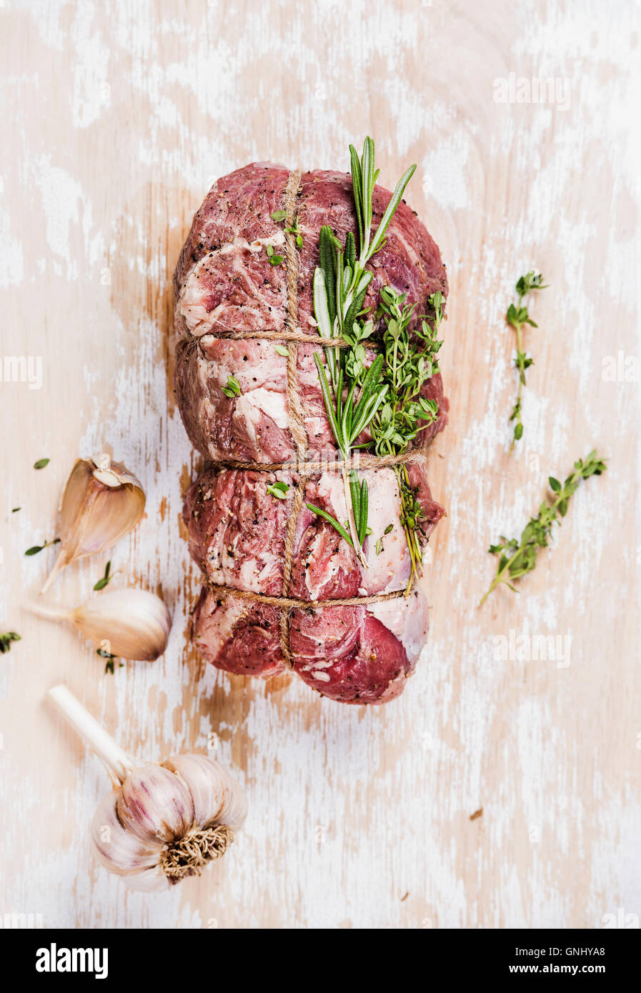 Raw uncooked roastbeef meat cut with rosemary, thyme and garlic on old white painted wooden background, top view, selective focu Stock Photo