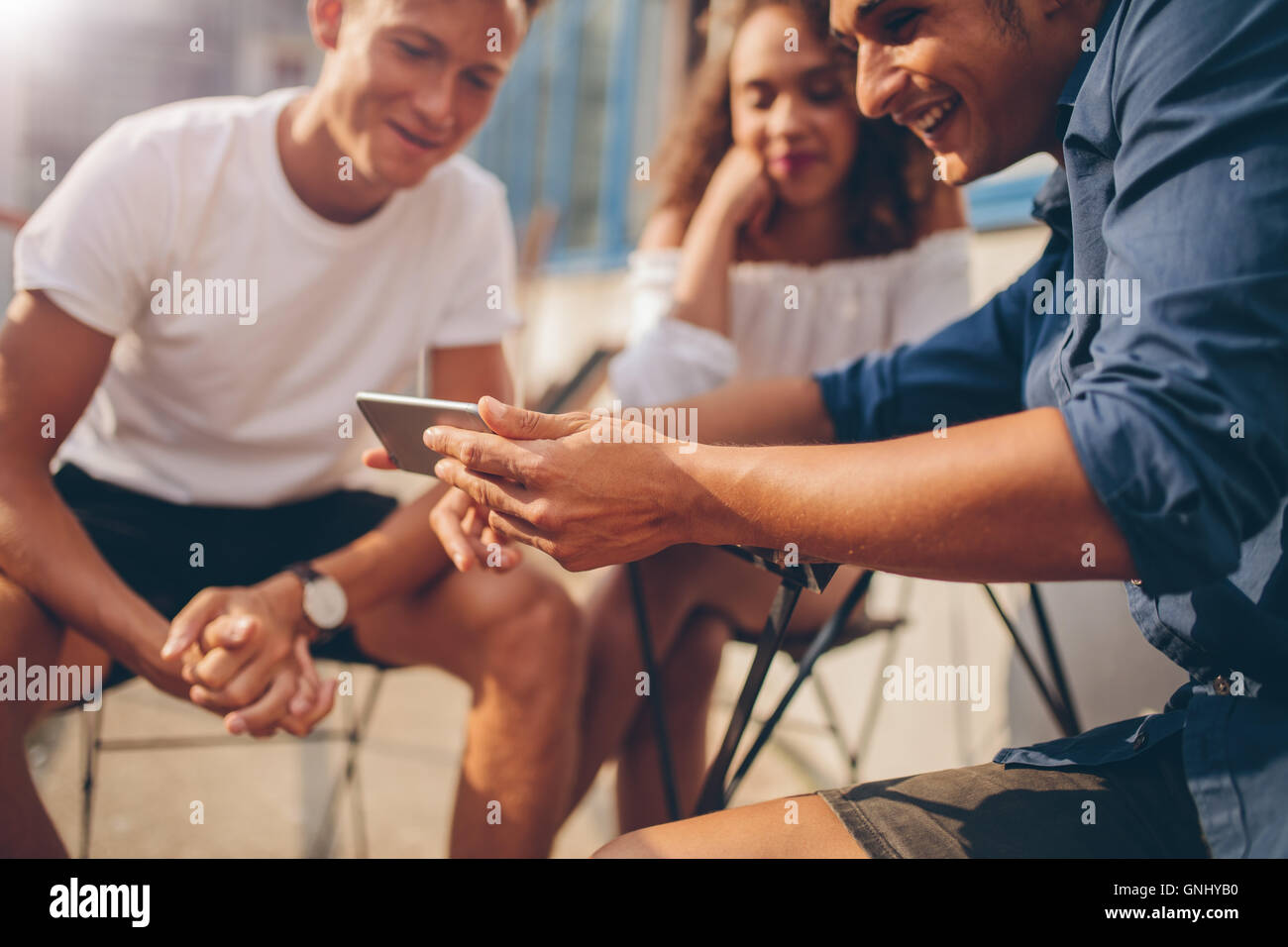 Young people sitting outdoors and looking at mobile phone. Group of friends sitting at outdoor cafe and watching video on the sm Stock Photo