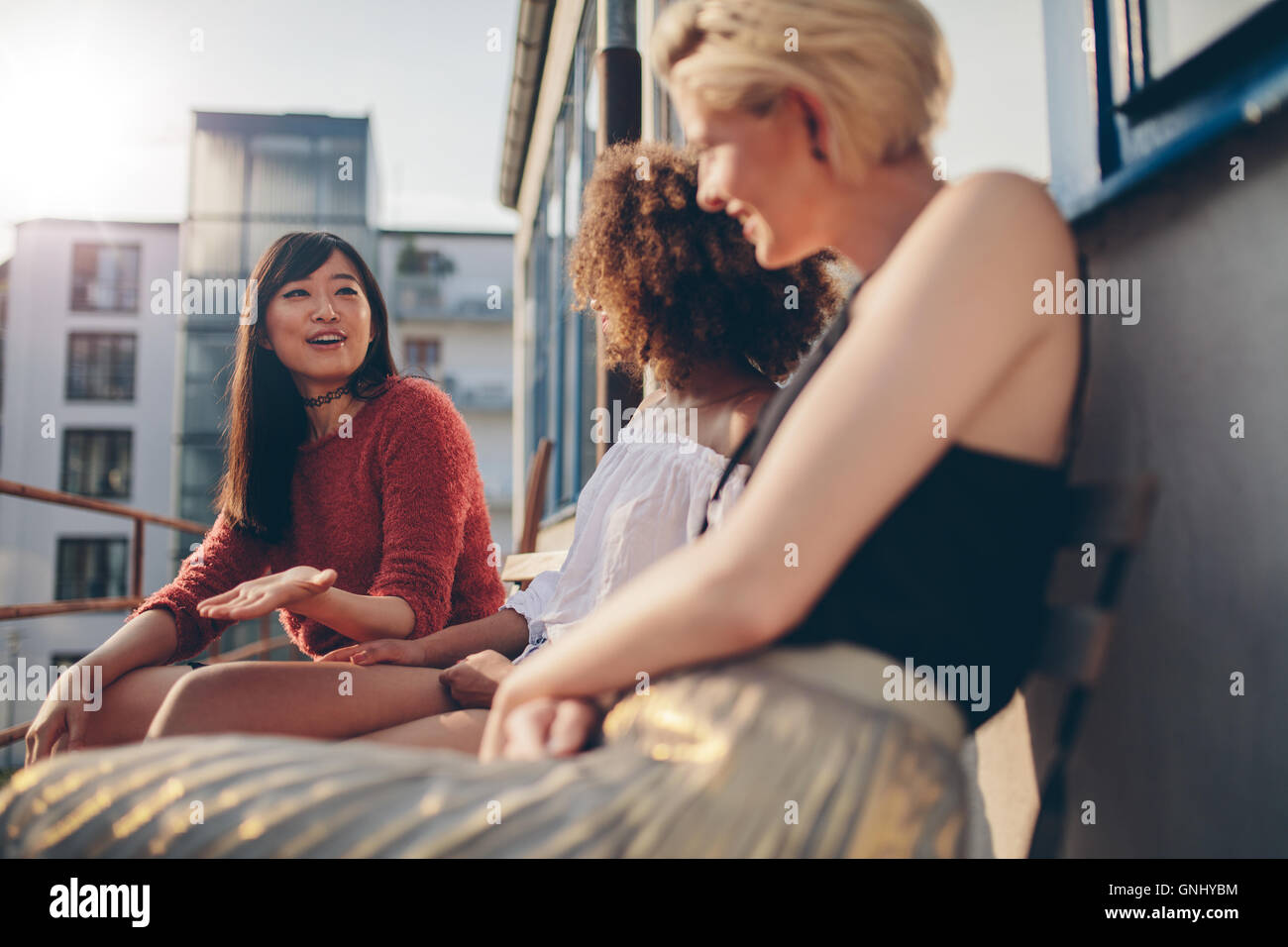 Shot of young female friends sitting together in terrace. Multiracial women relaxing outdoors in a balcony. Stock Photo