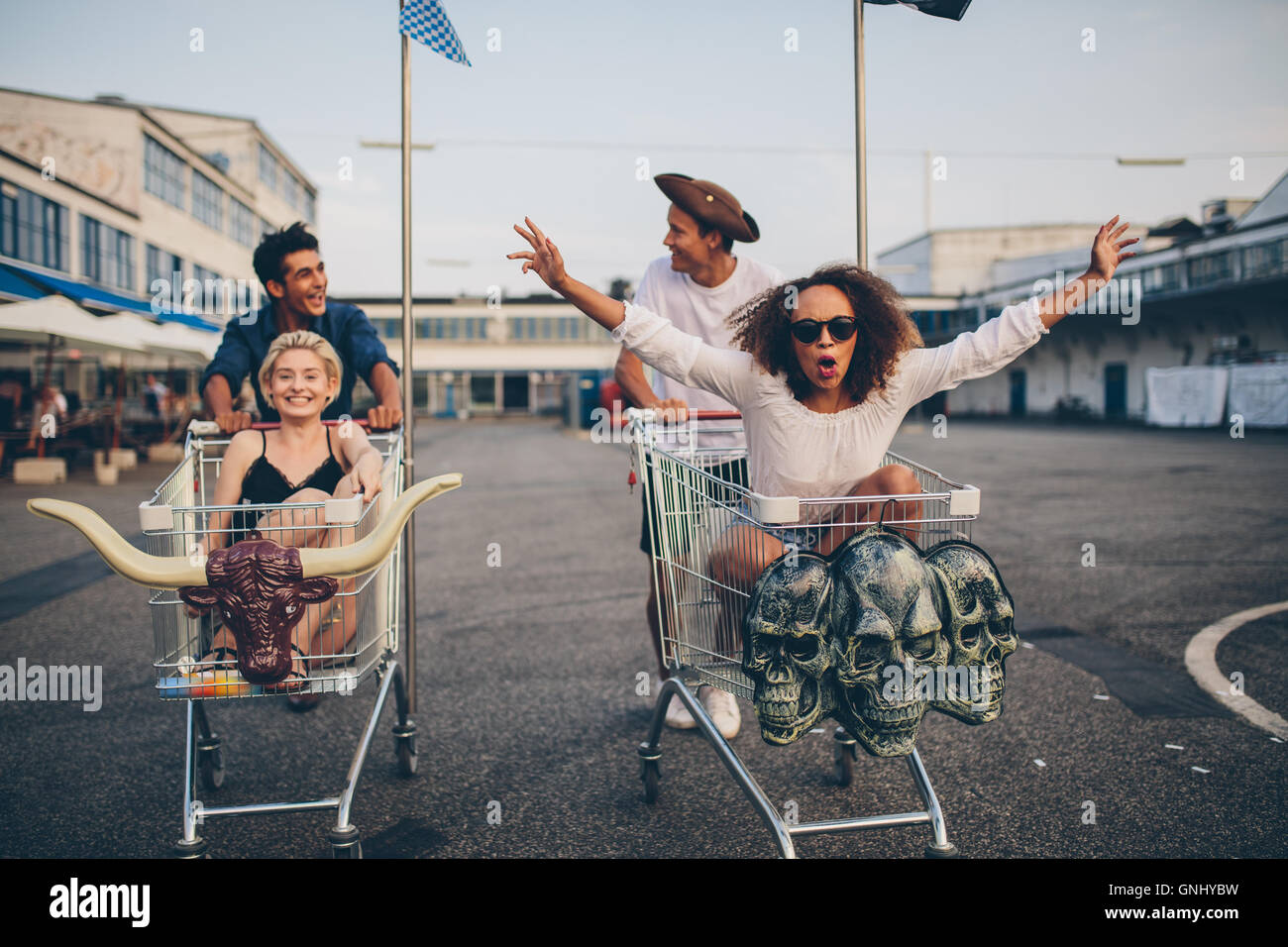 Young friends having fun on a shopping trolley. Multiethnic young people racing on shopping cart. Stock Photo