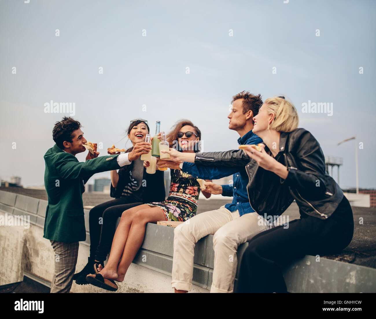 Multiethnic group of young adults on terrace, drinking and celebrating. Young men and women having drinks on rooftop party. Stock Photo