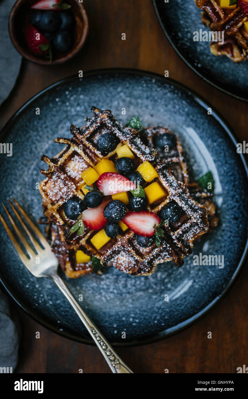 A plate of brioche waffles are topped off with fruit and dusted with powdered sugar photographed from the top view. Stock Photo