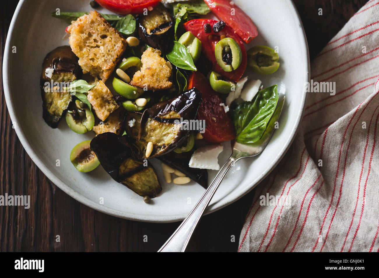 Roasted eggplant panzanella with capers, olives, and pine nuts, gluten-free. Stock Photo