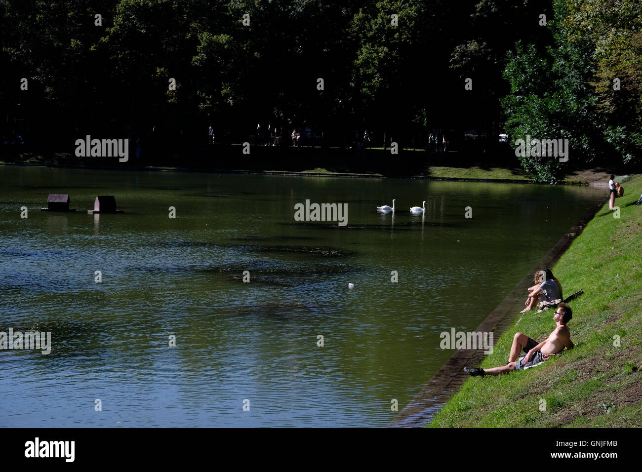 People sunbath as they sit at the bank of Patriarshiye Ponds or Patriarch's Ponds,  in Presnensky District of downtown Moscow, Russia. Stock Photo