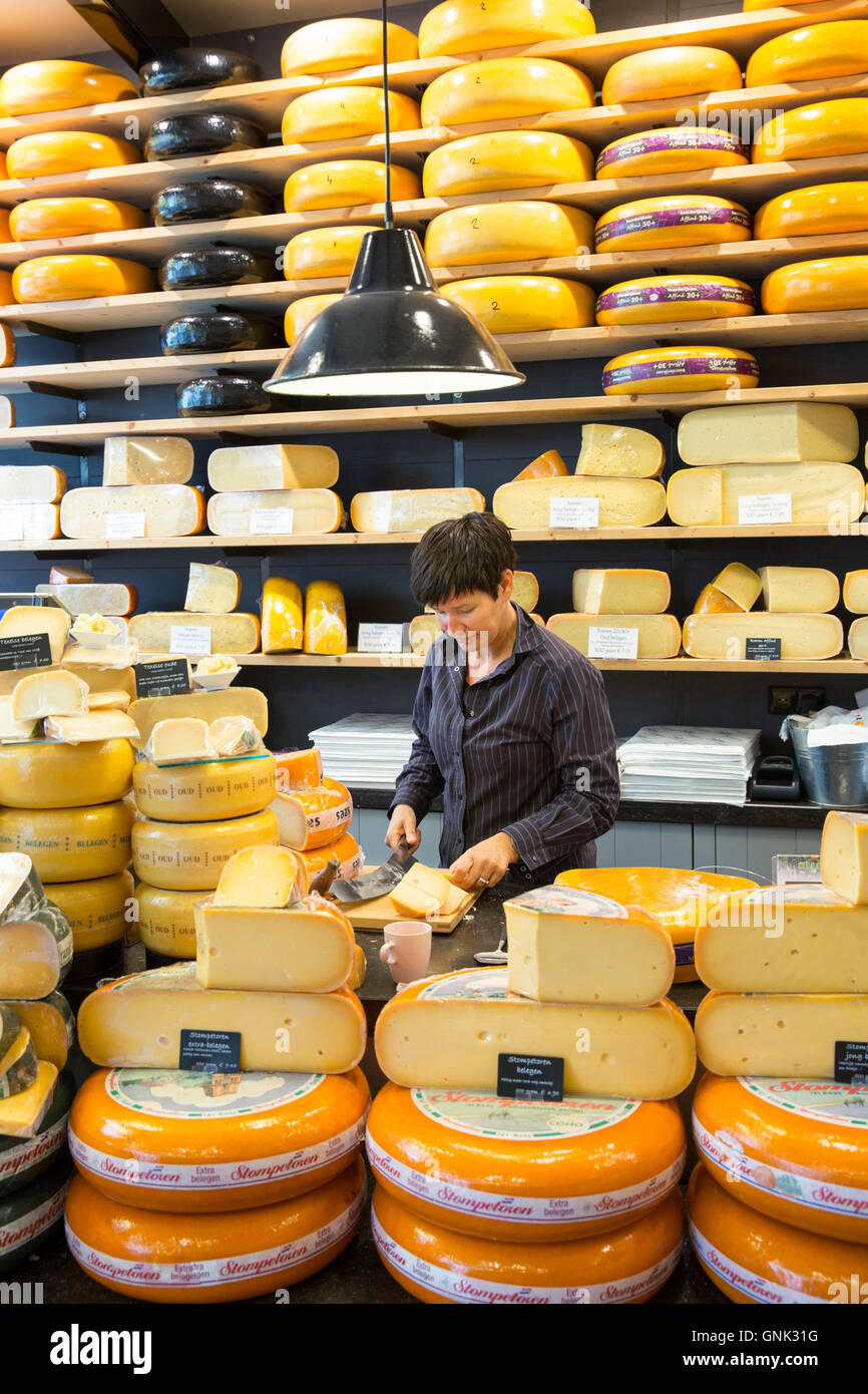 Shelves of cheese wheels and woman cutting cheese wedge at cheese shop