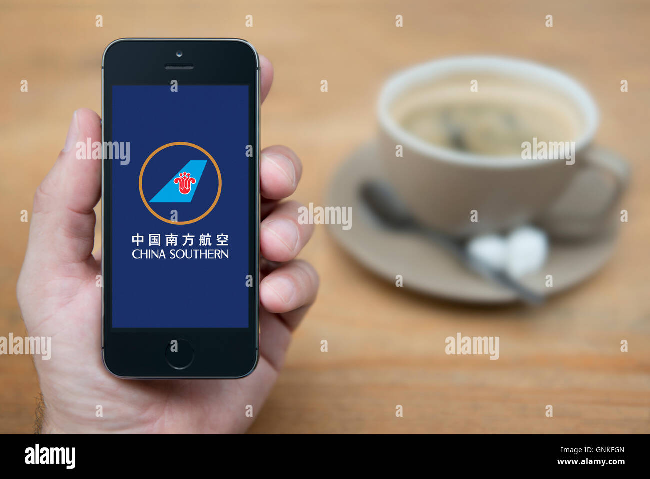 A man looks at his iPhone which displays the China Southern Airlines logo, while sat with a cup of coffee (Editorial use only). Stock Photo