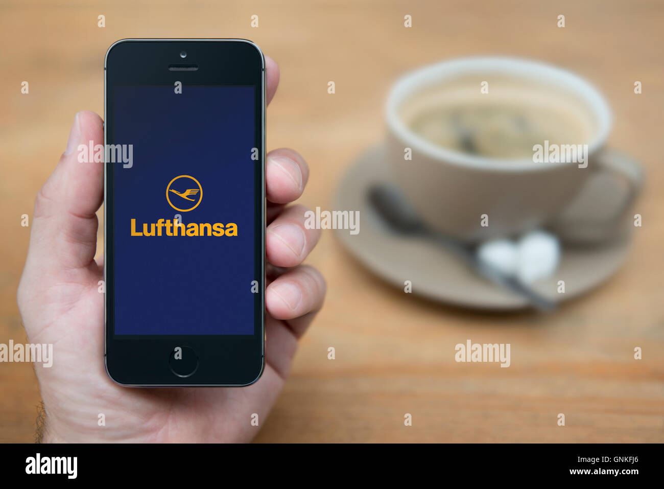 A man looks at his iPhone which displays the Lufthansa logo, while sat with a cup of coffee (Editorial use only). Stock Photo