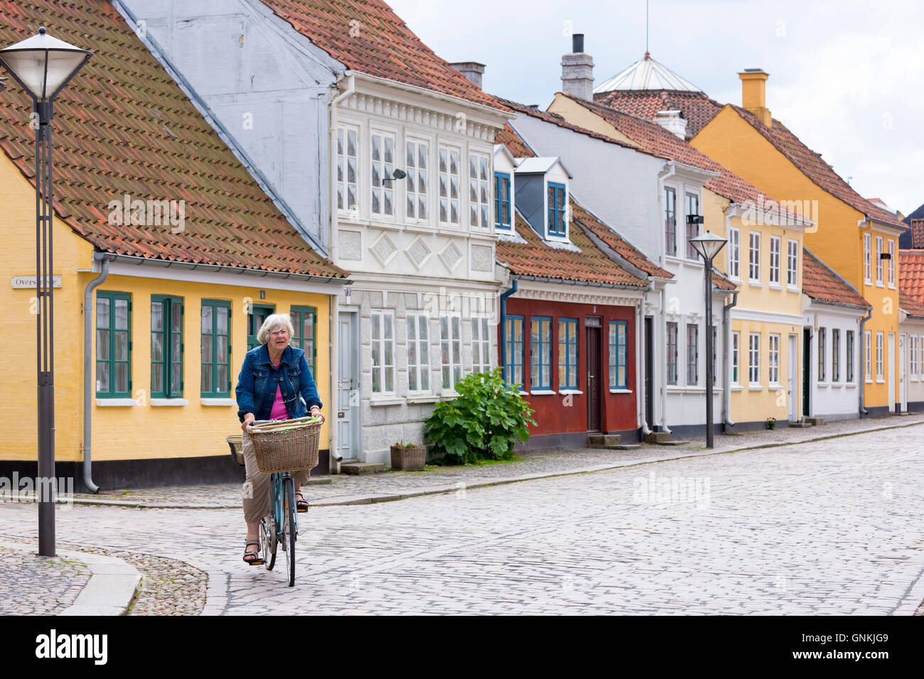 Woman cycling in Ramsherred cobbled street in old town in Odense on Funen Island, Denmark Stock Photo