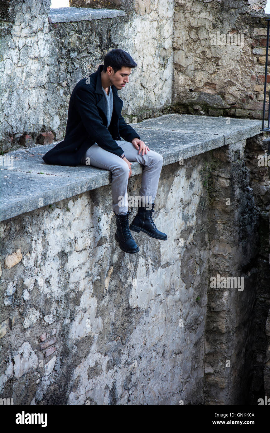 Portrait of good-looking man looking down while sitting on stone edge Stock Photo