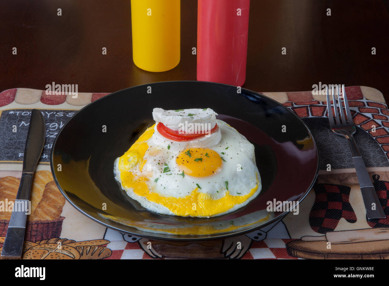 Fried Eggs, breakfast, mozzarella cheese, tomato, ketchup, mustard squeeze bottle, black plate Stock Photo