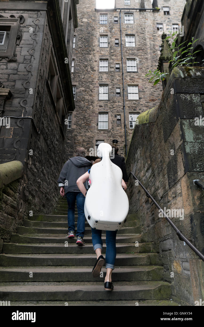 Musician carrying cello up narrow lane during Edinburgh Festival 2016 in Scotland, United Kingdom Stock Photo