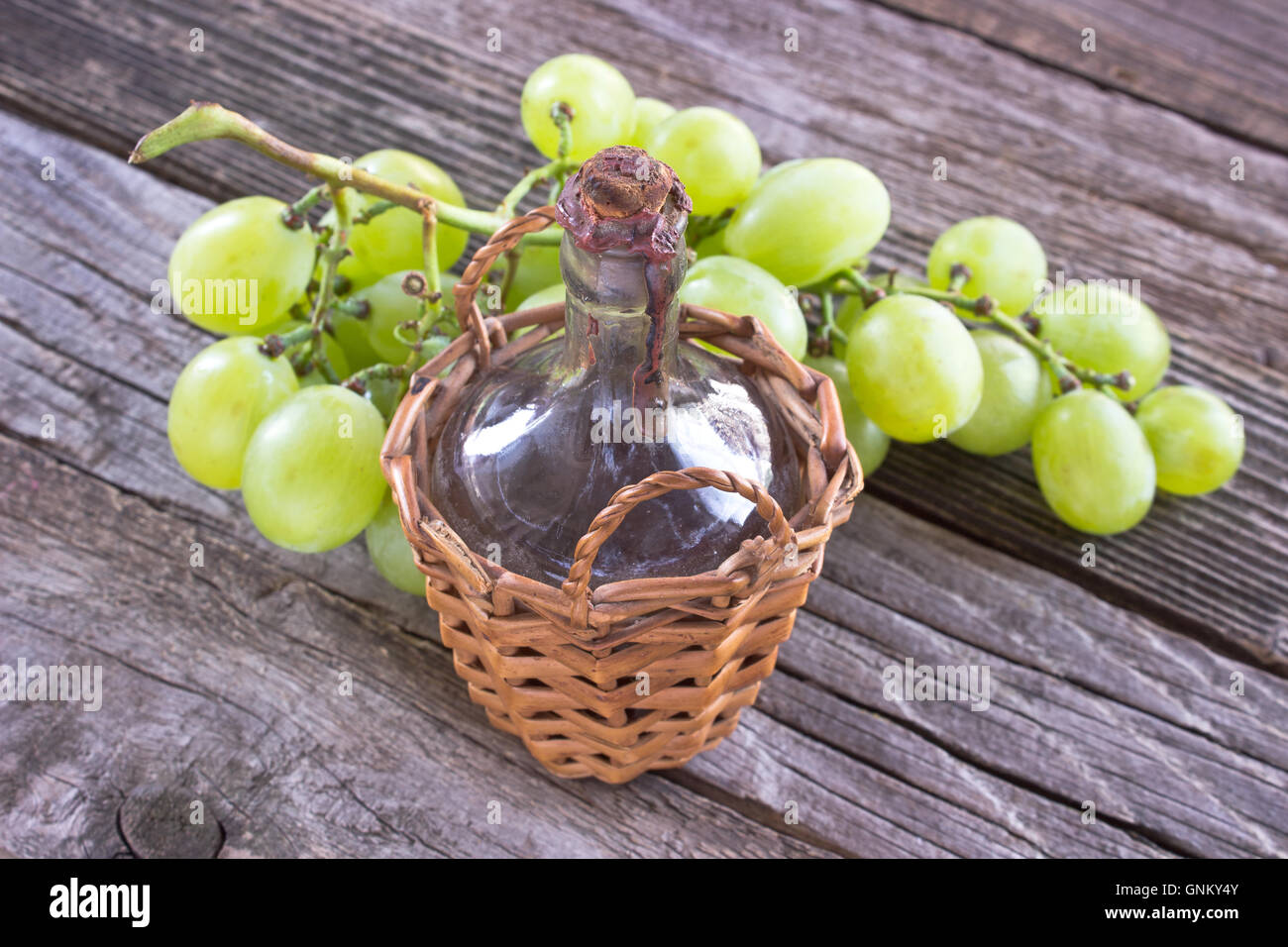 Old sealed bottle of wine and white grape on wooden background Stock Photo