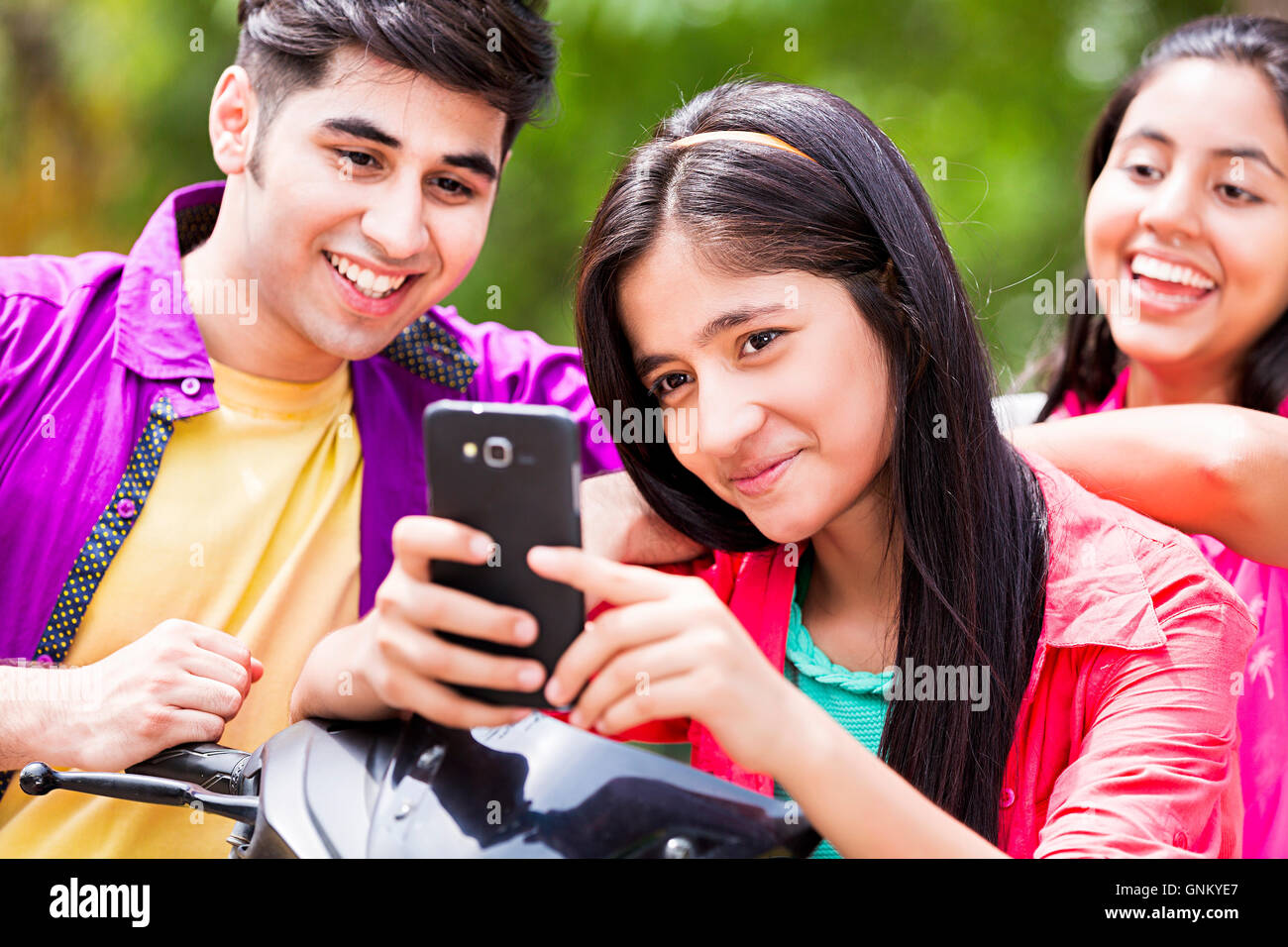 3 Young Girls and Boy  Friends Park sitting  Scooty and Chatting Mobile phone Stock Photo