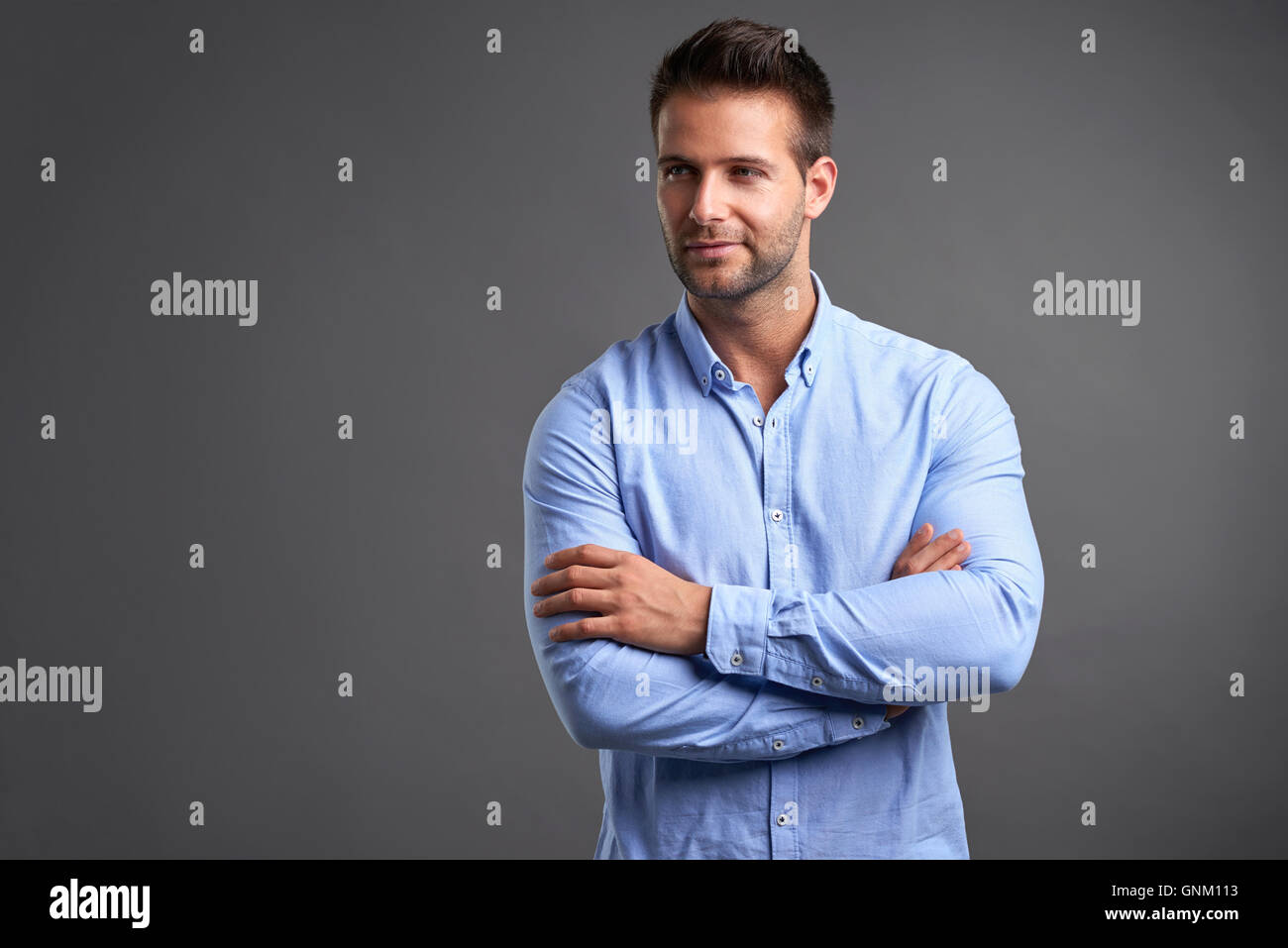 A confident handsome young man standing in front of a grey background ...