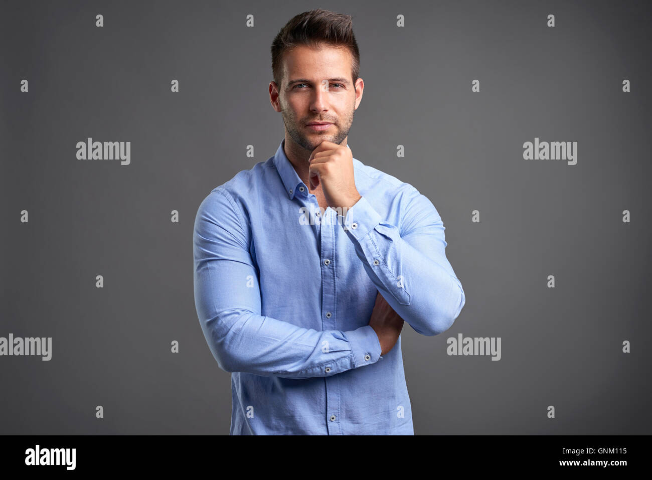 A confident handsome young man standing in front of a grey background ...