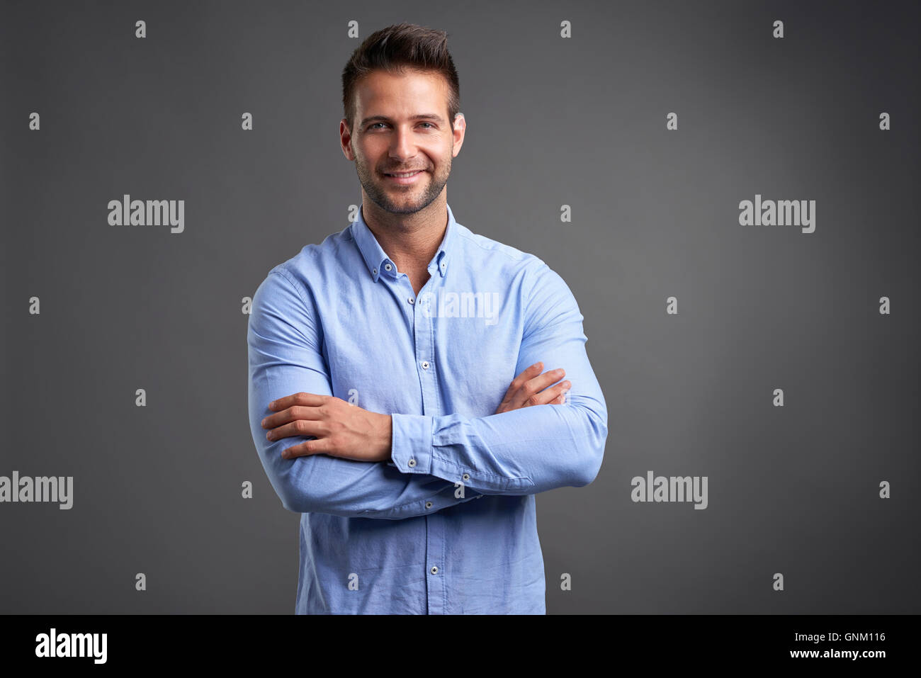 A confident handsome young man standing in front of a grey background ...