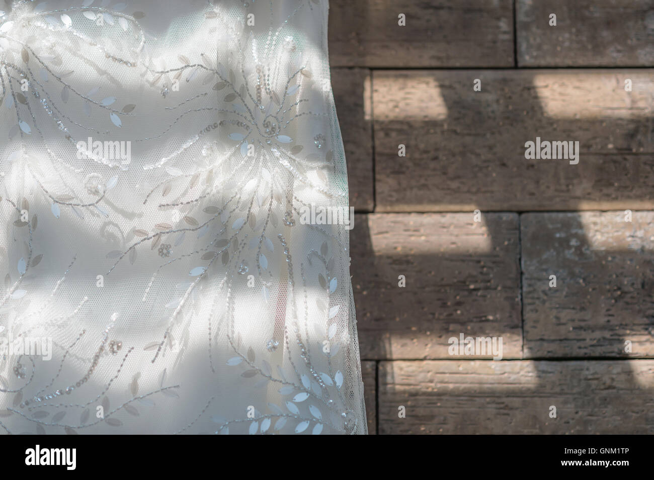 Wedding dress close up hanging on brown granite background, painted with light and shadow. Stock Photo