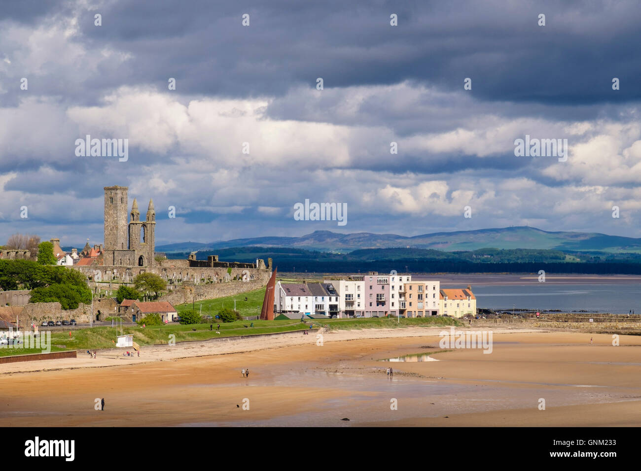 View across sunlit East Sands beach to Cathedral ruins in Scottish town under dramatic dark cloudy sky. St Andrews Fife Scotland UK Britain Stock Photo