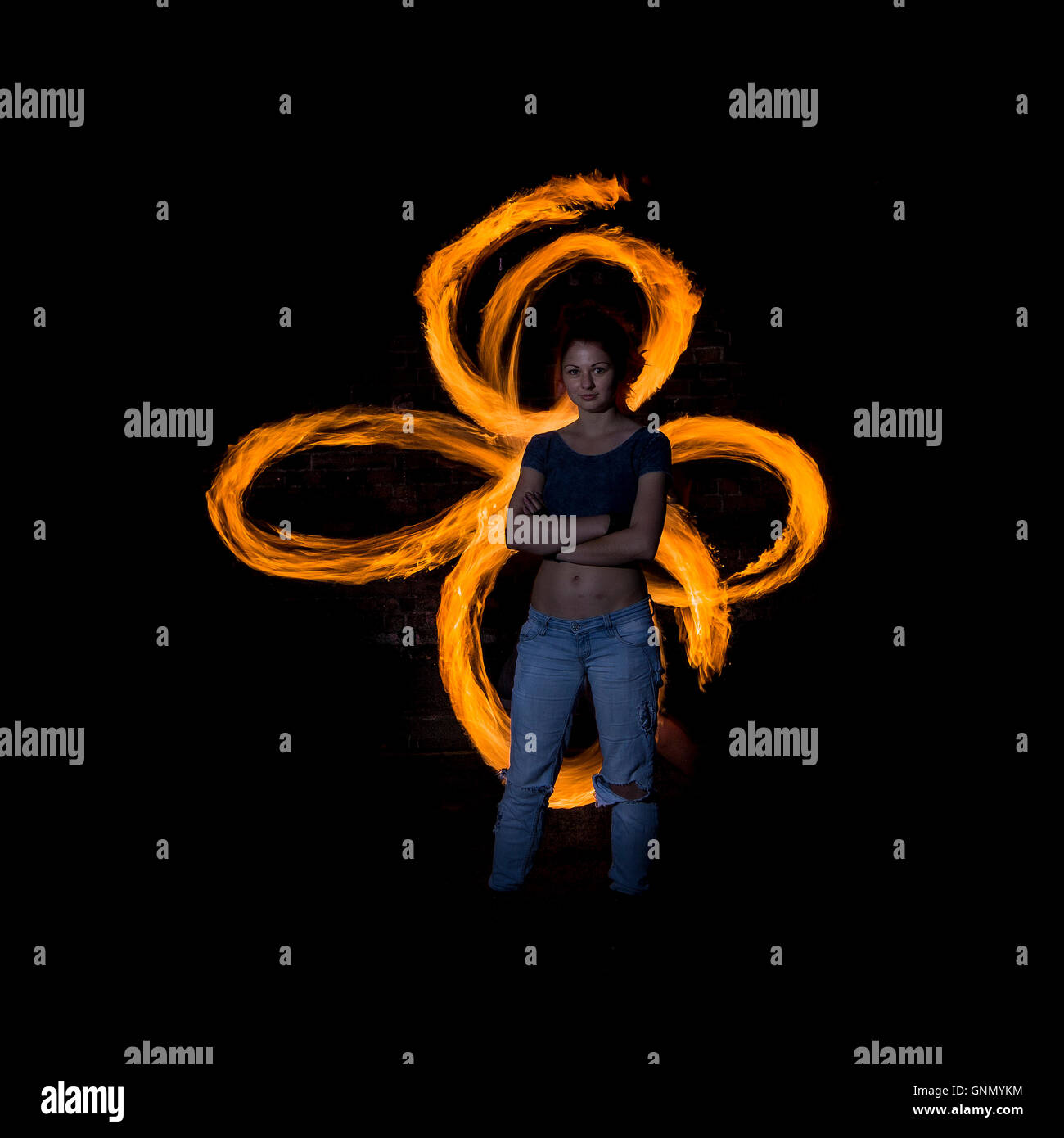 Female fire dancer poses silhouetted against intersecting rings of flame Stock Photo