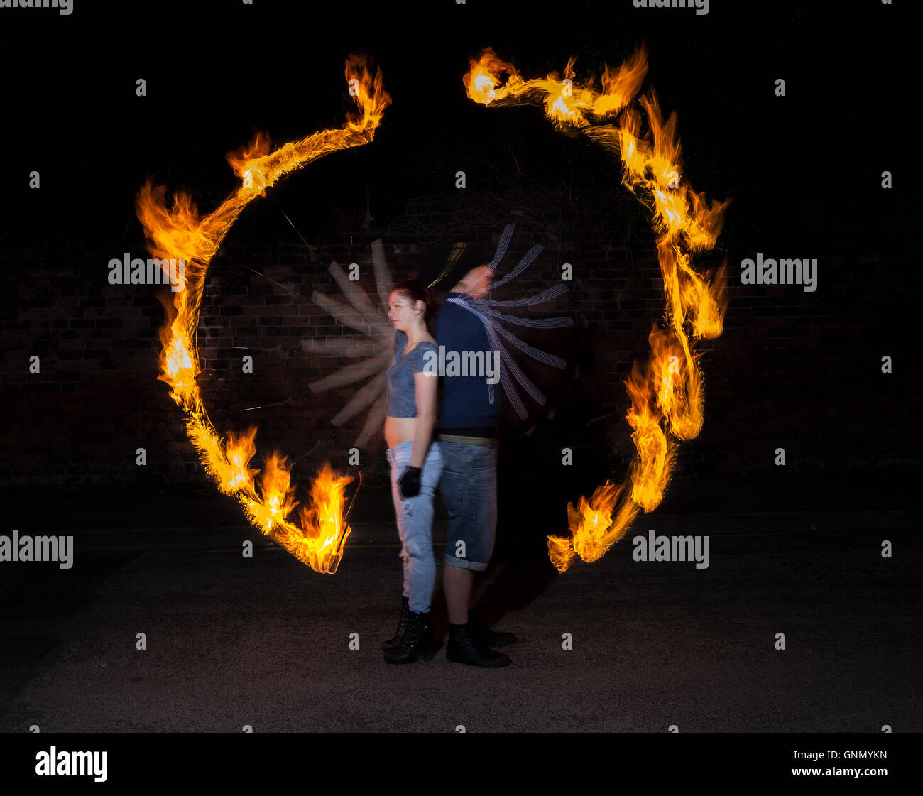 Two fire dancers spin poi in unison in darkness surrounded by ring of fire Stock Photo